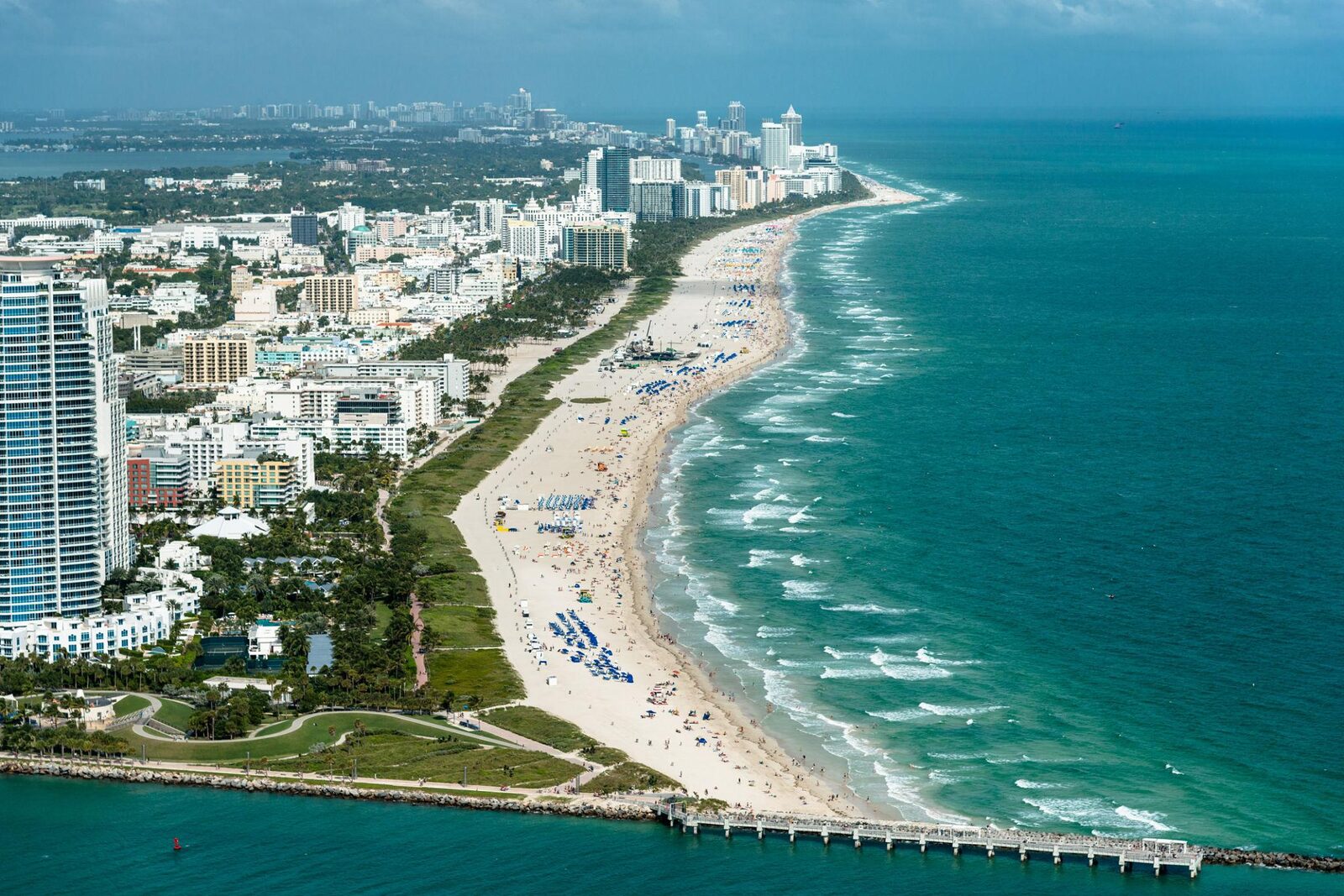 Aerial view of a long Miami beach filled with umbrellas, bordered by high-rises and the ocean