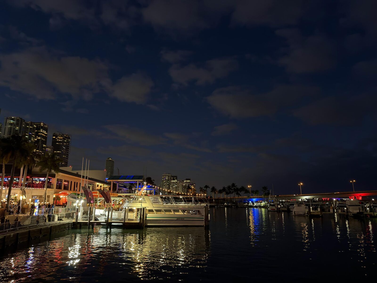 Nighttime view of boats docked at a waterfront pier with city lights