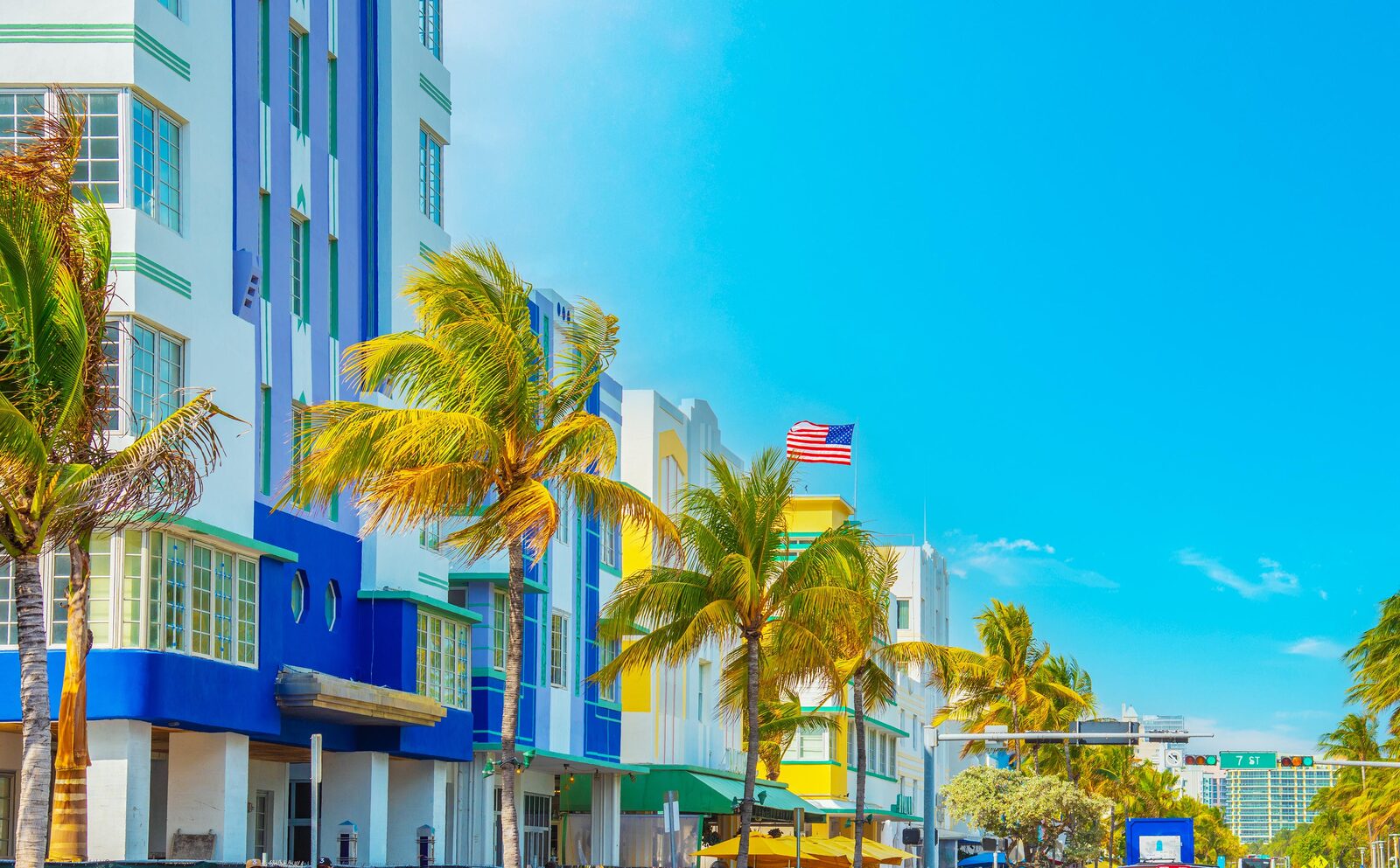 Row of vibrant blue and white Art Deco buildings with palm trees under a blue sky