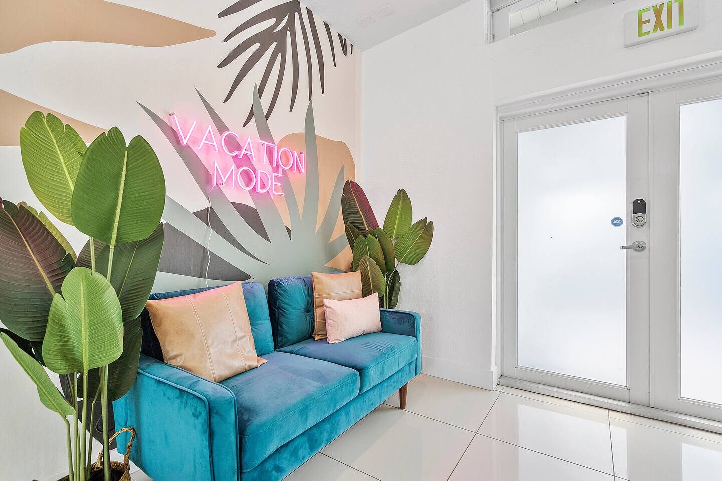 Teal velvet sofa with tropical mural and VACATION MODE neon sign